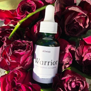 以下が含まれることがあります： 白いドロッパーと「adi.botany Warrior breast + lymphatic massage oil botanical and herbal infusion 30 ml | 1 fl oz」と書かれたラベルが付いた緑色のガラス瓶。瓶は乾燥した赤いバラで囲まれています。