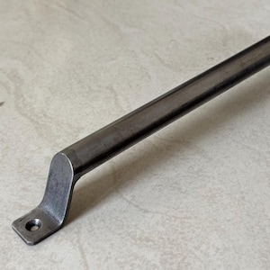 May include: A dark gray metal handle with a rectangular bar and curved ends. Each end has a small, flat plate with a single hole for mounting. The handle is designed for use on doors, drawers, or cabinets.