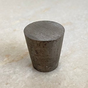 May include: A gray metal bottle stopper with a slightly conical shape. The stopper has a smooth, slightly textured surface.