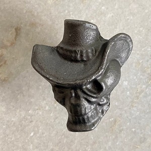Op de afbeelding: Een zwarte gietijzeren schedel met een cowboyhoed. De schedel is gedetailleerd ontworpen en de hoed heeft een brede rand.
