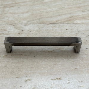 May include: A black metal cabinet pull with a rectangular shape and squared edges.