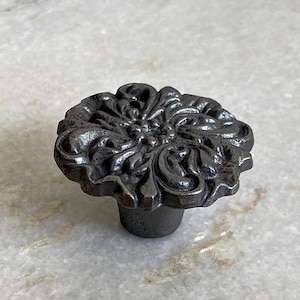 Può includere: Un pomello per armadio in ghisa nera con un design floreale.