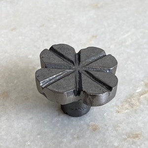 Puede incluir: Un pomo de armario de metal negro con un diseño geométrico con forma de flor.
