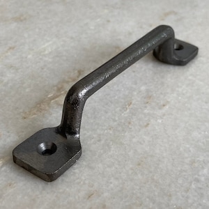 May include: A black metal cabinet pull with a rounded handle and square ends. The pull has two visible screw holes.