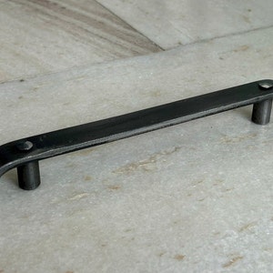 Könnte beinhalten: Schwarzer Metall-Schrankgriff mit abgerundeten Kanten und zwei kleinen runden Knöpfen.