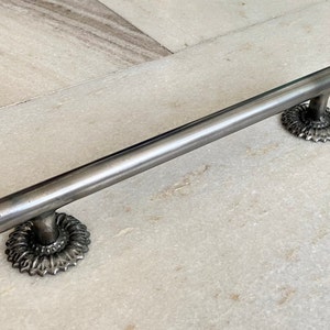 May include: A silver-toned metal cabinet pull with a cylindrical handle and decorative rosette-shaped base. The hardware is designed for easy installation and adds a touch of industrial style to furniture. The pull measures approximately 12 inches in length.