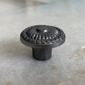 May include: A black cast iron cabinet knob with a decorative, raised, circular design.