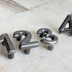 Könnte beinhalten: Satz mit vier Hausnummern aus Metall, 1, 2, 3 und 4, in silberner Ausführung. Die Zahlen sind im Vintage-Stil gestaltet und haben eine leicht abgenutzte Optik.