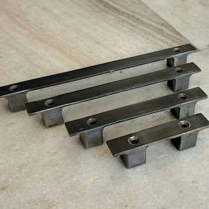 Può includere: Quattro maniglie per cassetti in metallo nero di diverse dimensioni. Le maniglie sono rettangolari con bordi arrotondati e hanno due fori per il montaggio.