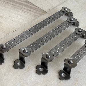 May include: Four black metal door handles with a decorative flower design on each end. The handles have a textured surface and are designed for use on doors.