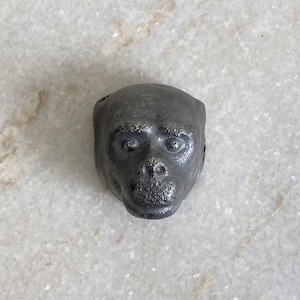 Può includere: Una scultura in ghisa nera a forma di testa di scimmia. La scultura è dettagliata con una superficie testurizzata e tratti realistici.