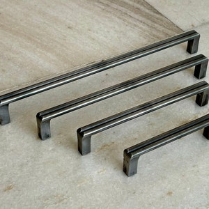 Puede incluir: Cuatro tiradores de armario de metal negro en diferentes tamaños. Los tiradores tienen una forma rectangular con un borde ligeramente redondeado y un diseño de doble línea.