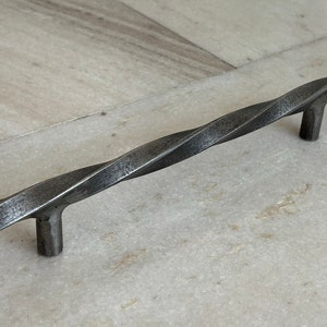 Op de afbeelding: Een gedraaide metalen kastgreep met een donkergrijze afwerking.