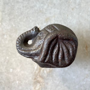 Op de afbeelding: Een donkergrijs metalen olifantenbeeldje met een gedetailleerd ontwerp. De slurf van de olifant is opgerold en zijn oren zijn groot en slap.