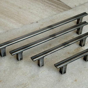 May include: Four silver metal cabinet pulls in various sizes. The pulls have a simple, modern design with two parallel bars.