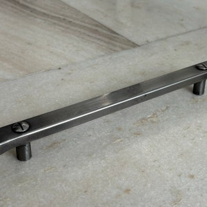 May include: A silver metal cabinet pull with rounded edges and two visible screws.