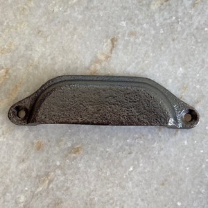 May include: A black cast iron drawer pull with a slightly curved top and rounded edges. The pull has a textured finish and two holes for mounting.