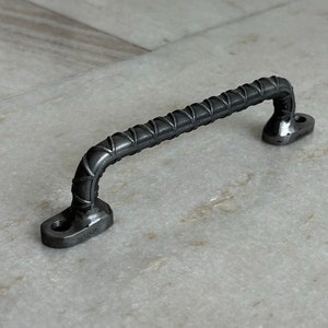 May include: A black metal door handle with a textured, ribbed design. The handle is curved and has a rounded shape at each end.