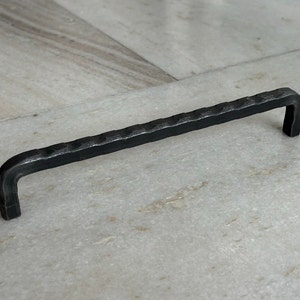 May include: Black metal cabinet pull with a hammered finish. The pull has a simple, rectangular shape with rounded edges.