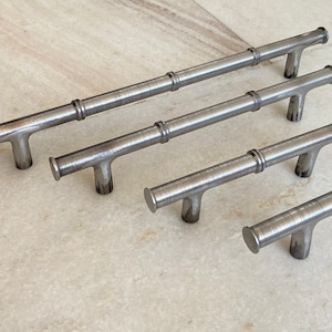Könnte beinhalten: Fünf silberne Metall-Schrankgriffe mit Bambus-Design. Die Griffe sind in verschiedenen Größen und in einer Reihe vom größten zum kleinsten angeordnet.