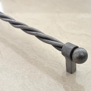 May include: A grey metal cabinet pull with a twisted rope design. The handle has a cylindrical shape with a ball-shaped end and a rectangular base. The hardware is made of a solid, durable metal.