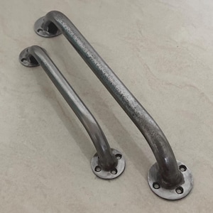 Peut inclure: Deux barres d'appui en métal avec une finition vieillie. Les barres sont incurvées avec des plaques de montage circulaires à chaque extrémité. La barre la plus grande mesure environ 30 cm de long, et la plus petite environ 20 cm.