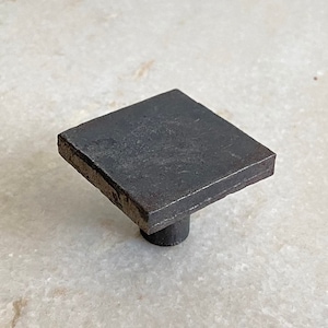 Peut inclure: Un bouton de porte carré en métal noir avec une texture légèrement rugueuse.