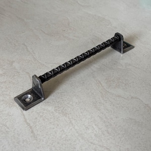 May include: A dark gray metal handle with a textured, ridged bar and square mounting plates. The handle is designed for a door or drawer and is made of a durable, industrial-style material.