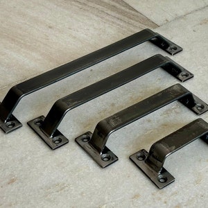 Puede incluir: Cuatro tiradores de puerta de metal negro de diferentes tamaños. Los tiradores son rectangulares con bordes redondeados y tienen un acabado mate.