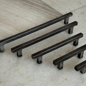 Peut inclure: Cinq poignées de tiroir en métal noir de différentes longueurs. Les poignées ont une forme rectangulaire avec une poignée en T.