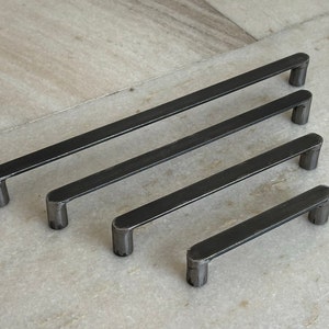 Könnte beinhalten: Drei schwarze Metall-Schubladengriffe in verschiedenen Längen. Die Griffe sind rechteckig mit abgerundeten Enden.