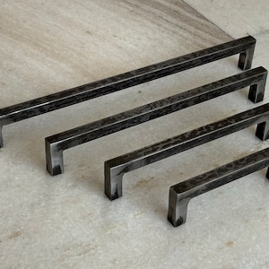 Peut inclure: Quatre poignées de tiroir en métal noir de différentes tailles. Les poignées ont une finition martelée et une forme rectangulaire aux coins arrondis.