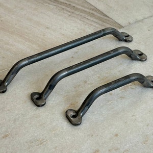 Könnte beinhalten: Drei schwarze Metall-Schubladengriffe in verschiedenen Größen. Die Griffe sind gebogen und haben ein schlichtes, industrielles Design.