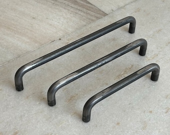 May include: Three black metal drawer pulls of different sizes. The pulls are all made of a simple, rounded design.