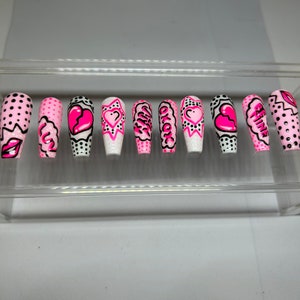 May include: Set of ten pink and white false nails with a comic book theme. The nails feature hearts, stars, and words like "Girl" and "Be Mine".