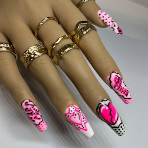 May include: Pink and white long press-on nails with black and pink designs. The designs include hearts, stars, and the words "Be Mine" and "Slay".