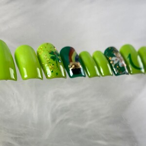 May include: A set of ten green and gold press-on nails with various designs, including shamrocks, a pot of gold, and a rainbow.