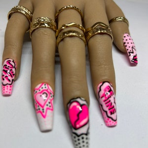 May include: Pink and white long false nails with different designs. One nail has a pink heart with a crack in it, another has a pink heart with a question mark, another has the words "Be Fine" in a pink speech bubble, and another has a pink and white polka dot design.