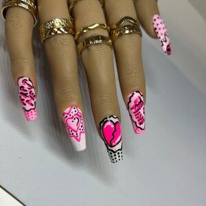 May include: Pink and white long, square-shaped acrylic nails with a comic book theme. The nails feature hearts, stars, and the words "Be Mine" and "Girl".