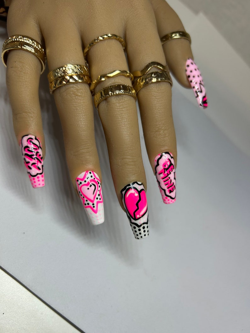 May include: Pink and white long, square-shaped acrylic nails with a comic book theme. The nails feature hearts, stars, and the words "Be Mine" and "Girl".