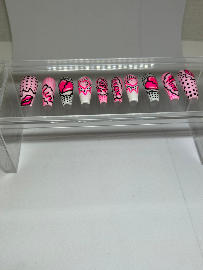 May include: Set of ten pink and white false nails with various designs including hearts, polka dots, and the words "Girl Power".