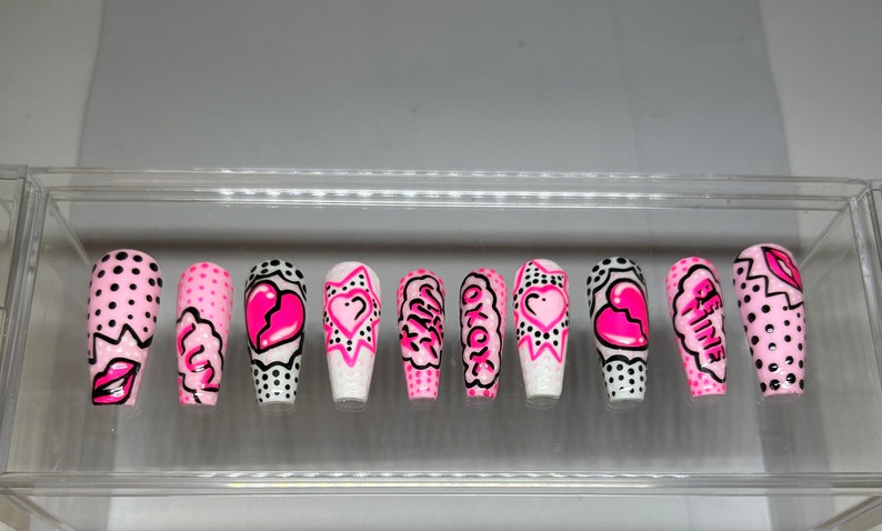 May include: Set of ten pink and black false nails with various designs. The designs include hearts, polka dots, and words like "Girl" and "Be Mine".