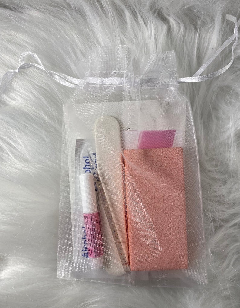 May include: A white organza bag filled with nail care supplies. The bag contains a nail file, a pink nail buffer, and a small bottle of alcohol.