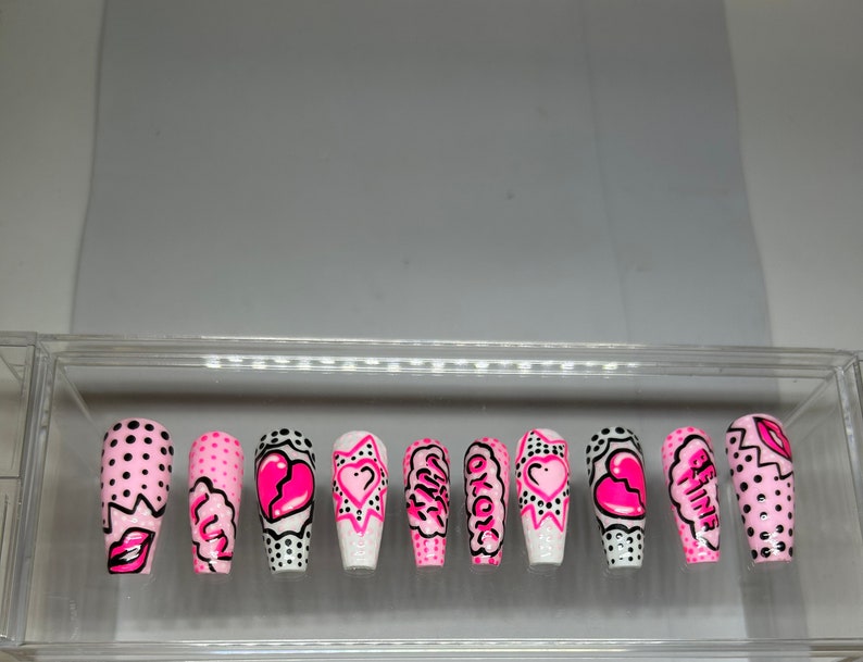 May include: Set of ten pink and white false nails with different designs. Some nails have black polka dots, a broken heart, a star, and the words "Okay" and "Be Fine".