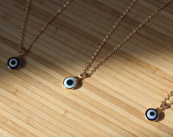 Puede incluir: Tres collares de oro con colgantes de ojo turco azul y blanco sobre una superficie de madera.