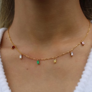 May include: A gold chain necklace with colourful rectangular gemstones hanging from it. The gemstones are red, green, yellow, and pink.