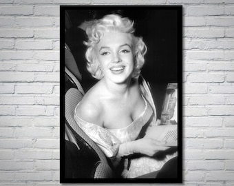 May include: Black and white portrait photograph of a woman with blonde hair smiling. She is wearing a low-cut, off-the-shoulder dress and is holding a piece of paper.