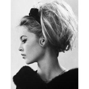 May include: Black and white portrait photograph of a woman with her hair styled in a bouffant. She is wearing a black fur collar and a black headband.