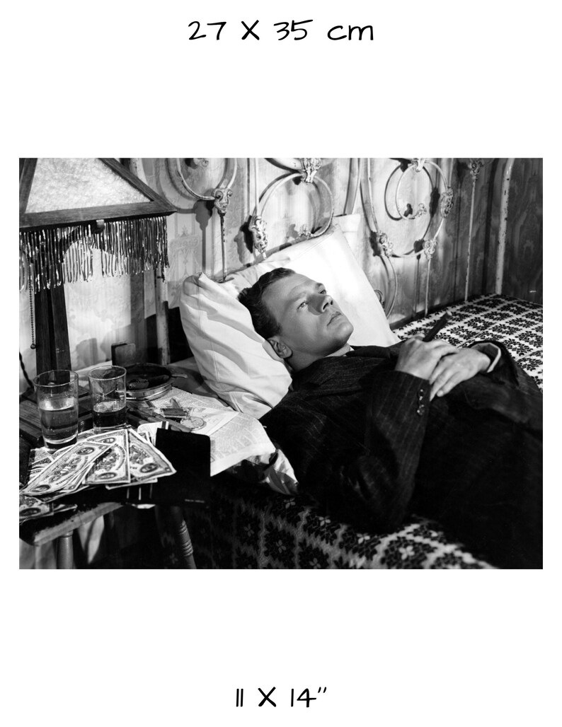 K&ouml;nnte beinhalten: Schwarzwei&szlig;foto eines Mannes, der im Bett liegt. Er tr&auml;gt einen Anzug und hat die H&auml;nde auf der Brust gefaltet. Auf einem Tisch neben dem Bett stehen Gl&auml;ser und Geld.