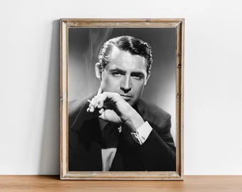 May include: A black and white framed portrait of Cary Grant wearing a dark suit with a white shirt and cufflinks. The subject is shown from the chest up, with one hand raised near the face holding a cigarette, with visible smoke rising upward.